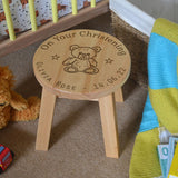 A personalised wooden stool in a children's size. The stool has a design engraved on the wooden seat which features text in a circle around the outside with a teddy bear in the middle.