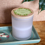  A close up of the bamboo lidded candle with a message printed in green ink on the lid. The lid also has a circle of green leaves and a light green background.