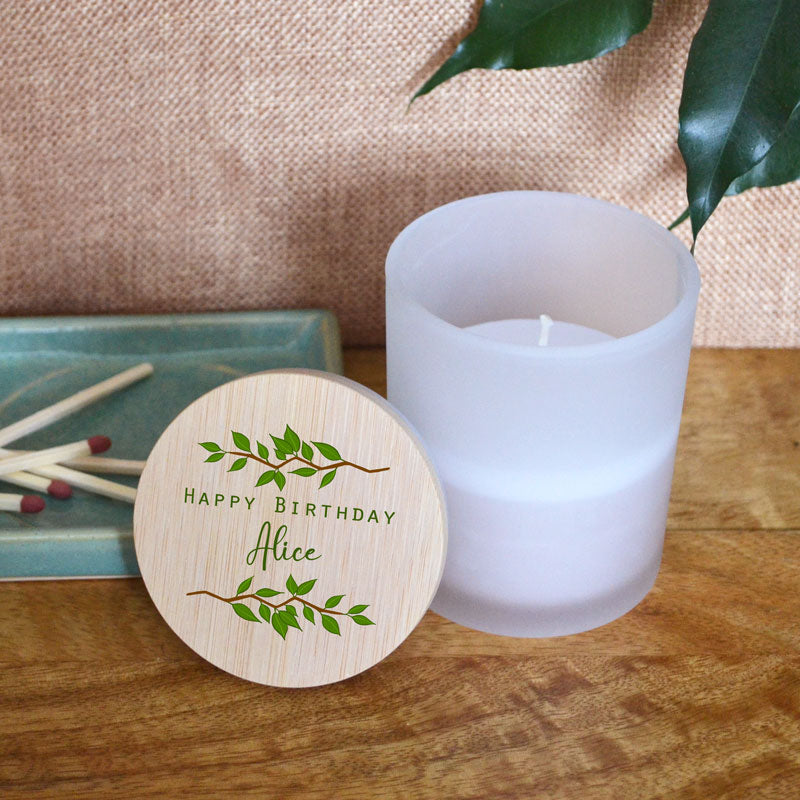 A personalised birthday candle in a glass jar with a bamboo lid. The bamboo lid is printed with a leaf pattern and the words 