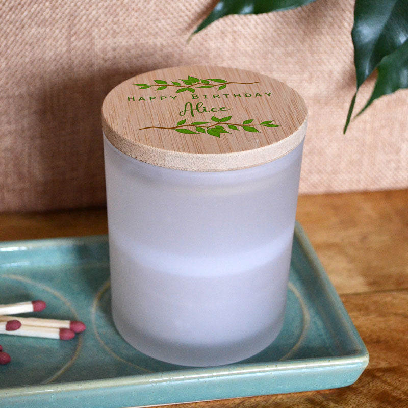 A view of the birthday candle with its bamboo lid on top. The Bamboo lid has two branches of green leaves surrounding the words 