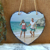 A personalised photo heart shaped slate plaque with rustic string for hanging on a wall.