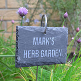 A personalised slate garden sign with the words "Mark's Herb Garden" engraved on it.