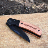 A personalised pocket knife displayed outdoors on a wooden board with the blade visible.
