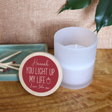 A personalised Valentine's Day candle with the message "You light up my life" printed on the lid. the candle is in a glass jar with a bamboo lid. The text is in white on a dark pink background and you can add a name and message.