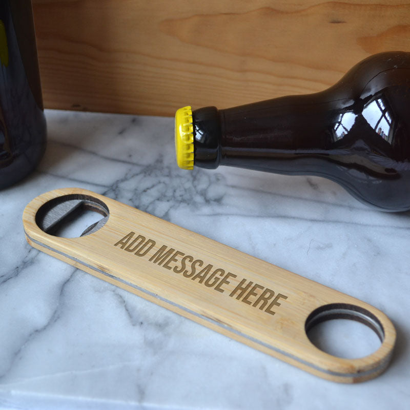 A bamboo bottle opener with a hoop at one end  engraved with a personal message, ideal for a birthday gift. Pictured on a marble top with a beer bottle.