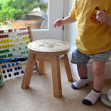 A personalised wooden stool in a children's size. The stool has a design engraved on the wooden seat which features text in a circle around the outside with a teddy bear in the middle.