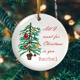 A personalised circular ceramic Christmas decoration with an illustration of a Christmas tree and the words "All I want for Christmas is you Rachel" in red script text printed onto it.