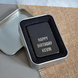 A personalised black lighter in a metal tin with a birthday message engraved on the front