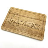 Personalised wood Christmas chopping board, engraved with a festive design including a Christmas tree and the words, "The Wilson Family, Christmas Cheese Board". Pictured on a white background.