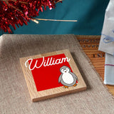 A personalised Christmas coaster in solid oak with a name and a penguin printed on the front.
