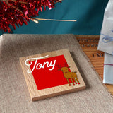 A personalised Christmas coaster in solid oak with a name and a reindeer printed on the front.