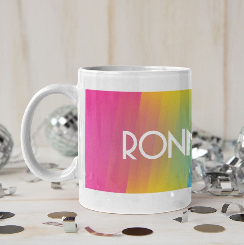 A personalised white ceramic 10oz mug, surrounded by silver confetti and mini disco balls.  The mug has a pansexual flag (pink, yellow and blue) and a name in the centre in white. 