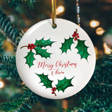A personalised white ceramic decoration. The decoration is printed with a holly pattern and has the words "Merry Christmas Olivia" in red lettering in the centre