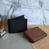 Two personalised leather wallets, on in black and one in brown. Both wallets have a name engraved on the front. 