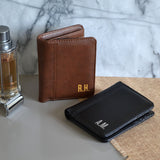 Two personalised wallets on a side table with aftershave an a razor. One wallet is brown and one is black, both have custom initials printed on them.