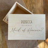 A personalised maid of honour gift box which is made from natural wood. The lid is engraved with a name and the question "Will you be my Maid of Honour?".