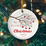 A personalised Christmas bauble celebrating a child's first Christmas. The design includes a winter tree decorated with gold stars and red baubles.