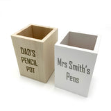 Personalised wooden pencil pots pictured on a white background. One has a natural finish and the other is matt white. Complete with different messages engraved on to the front.