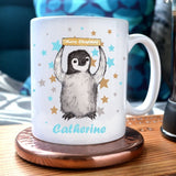 A personalised mug with an illustration of a baby penguin holding a sign which reads "Merry Christmas". The name Catherine is printed below the penguin. 