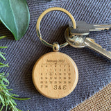 A personalised wooden keyring in a circle shape. The wooden disk is engraved with calendar month with a special date circled. The design also features initials of your choice.