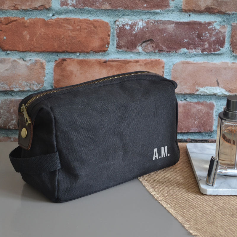 A personalised black wash bag in waxed cotton with silver custom initials printed on the front