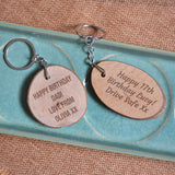 Two personalised tree slice keyrings with custom messages. One keyring is oval shaped, and one is round. Both have a custom message engraved on the font.