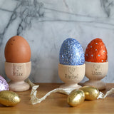 Three personalised wooden egg cups with boiled eggs and chocolate eggs sitting in them