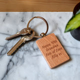 Image of a solid beech keyring with a couple of keys. It has the message "Happy 70th Grandma Lots of Love Lilly xx" engraved on the wooden tag.
